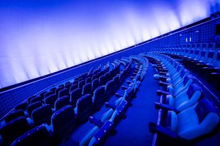 Our Planetarium seats, seen from the side on. The screen is also brightly lit up, with a blue hue.